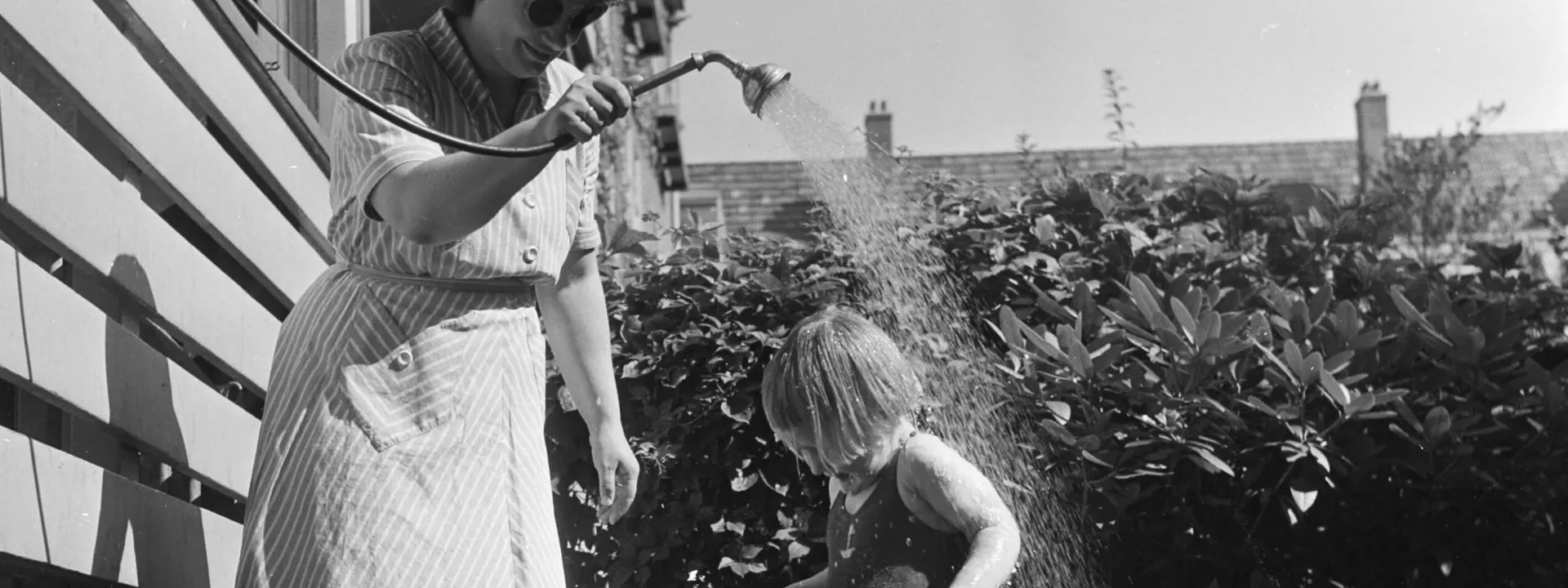 Vrouw geeft kind geïmproviseerde douche buiten in een ton